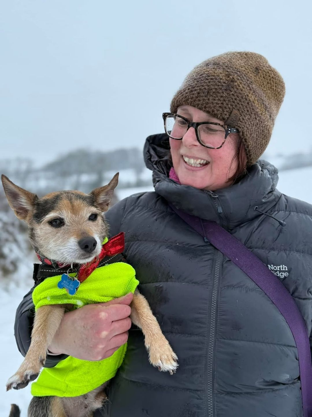Catherine smiling outdoors, holding a dog in winter clothing